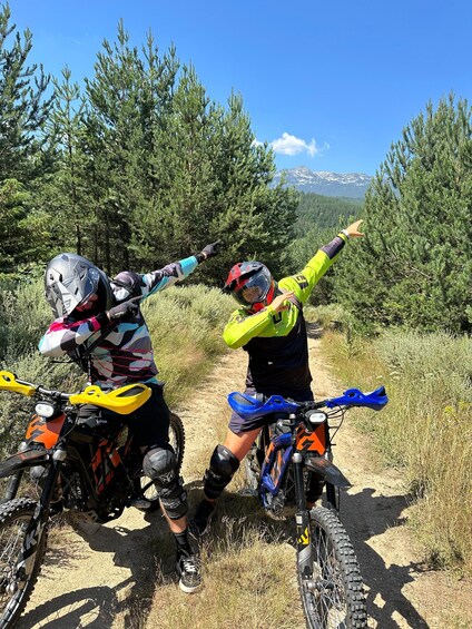 Two motorcyclists on a dirt trail with trees and mountains in the background. 4
