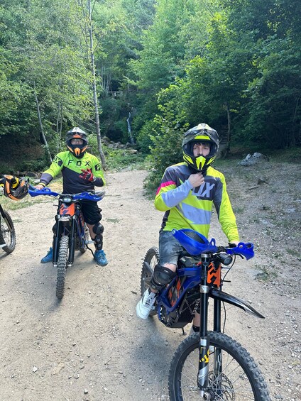 Two people on mountain bikes on a dirt trail surrounded by trees. 2