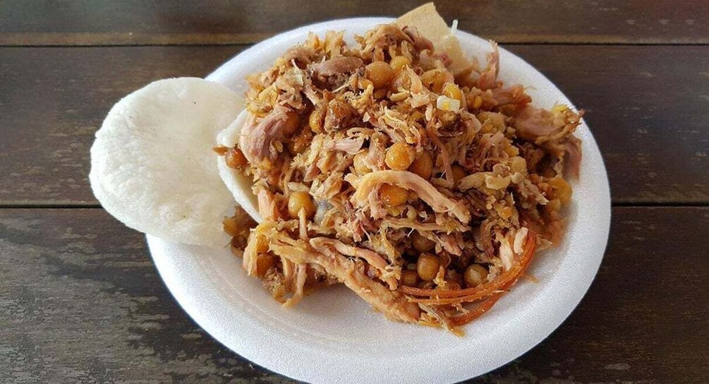 A plate of shredded meat with chickpeas and a white bread-like item on a wooden table. 4