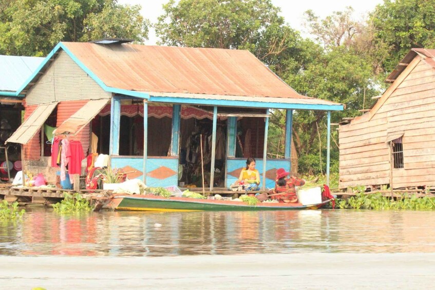 A wooden house with a blue roof and a boat docked in front, with people sitting on the boat. 1