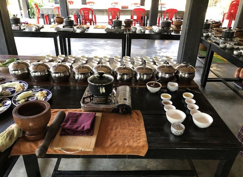 A traditional cooking setup with multiple pots and bowls on a table, surrounded by red chairs. 4