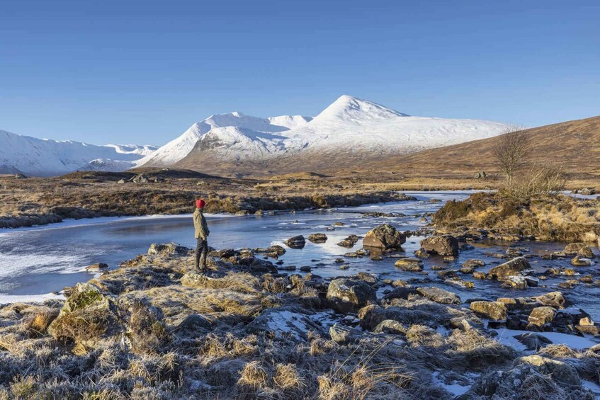 A snowy landscape with a river, rocks, and a person standing by the water. 1
