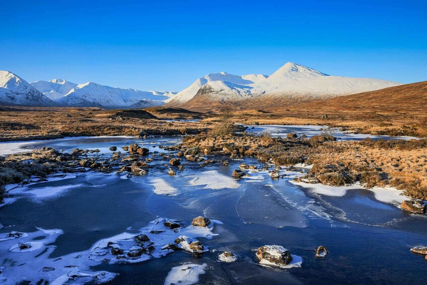 A frozen river with snow-covered rocks and mountains in the background. 3