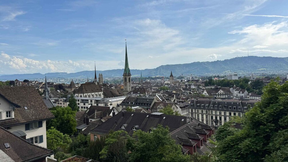 A cityscape with a prominent church spire, dense residential buildings, and a mountainous backdrop. 2