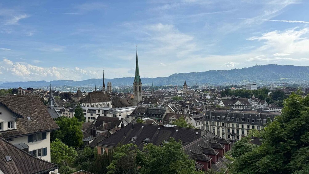 A cityscape with historic buildings, a prominent church spire, and a mountainous backdrop. 4