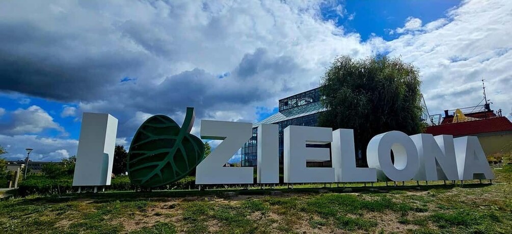 A sign with the word 'IZIELONA' in large letters, a modern building, and a partly cloudy sky. 1