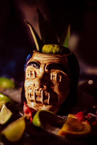 A carved wooden mask with a green leaf on top, surrounded by lime and red fruit slices. 4