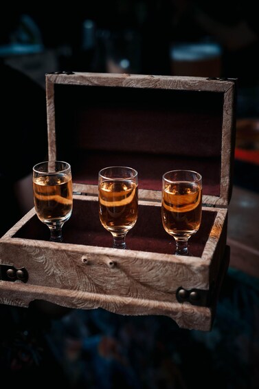 A wooden box with three glasses of amber liquid. 5