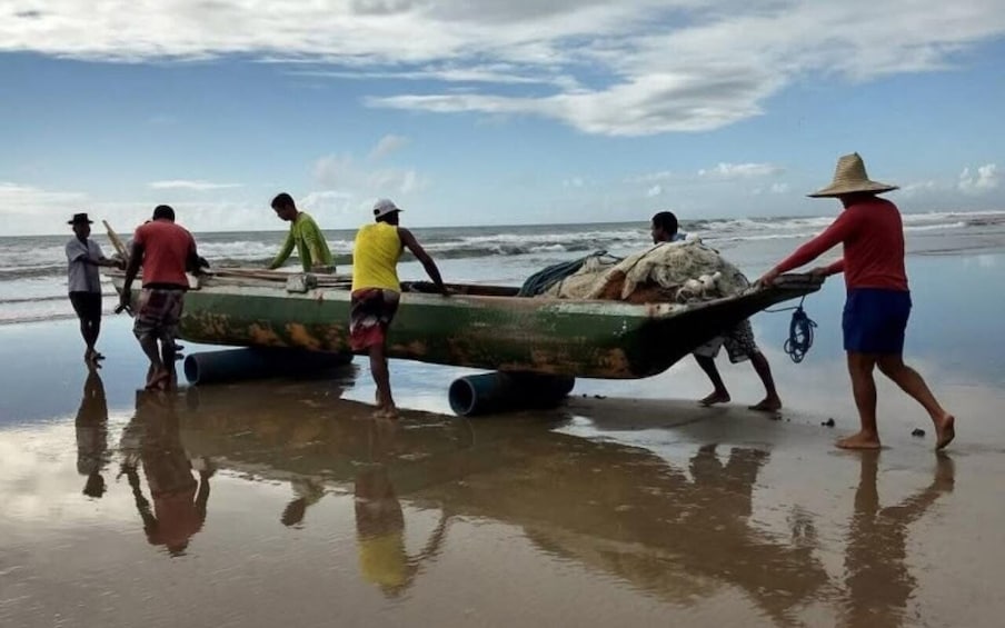 People pulling a boat on a wet beach with the ocean in the background. 5