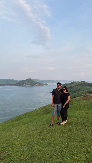 Two people standing on a grassy hill overlooking a body of water with distant landforms. 4