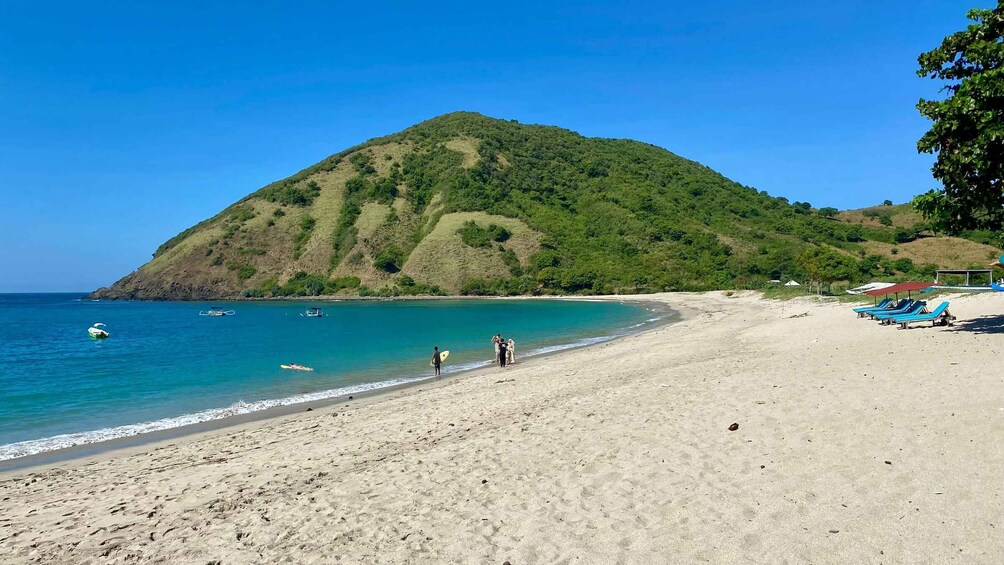 A beach with clear turquoise water, a sandy shore, and a green hill in the background. 5