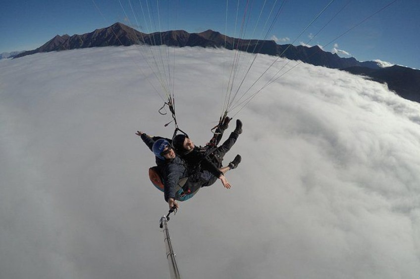 En person paraglider over skyer med bjerge i baggrunden. 2