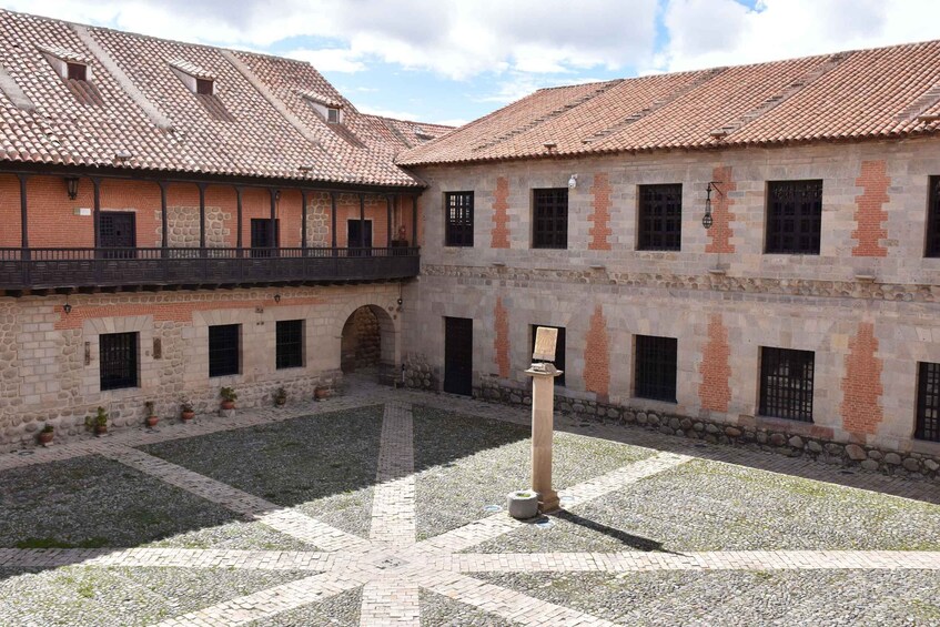A courtyard with tiled roofs, brick buildings, and a central column. 3