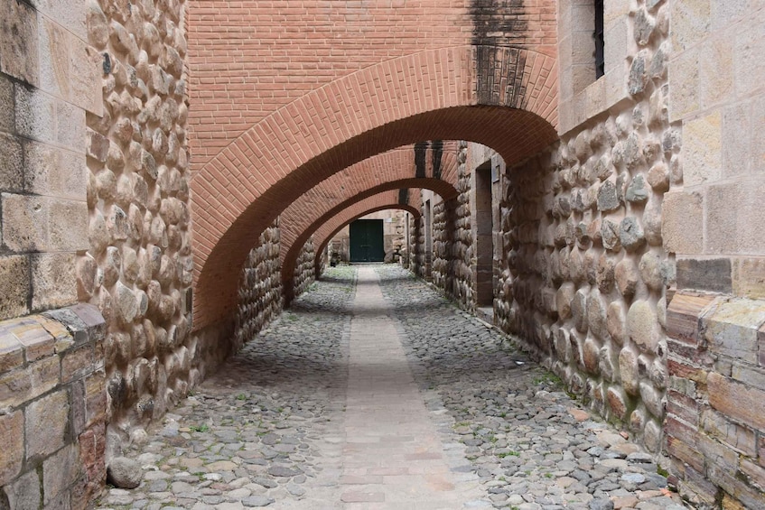 A narrow cobblestone alley flanked by stone walls and brick arches. 2
