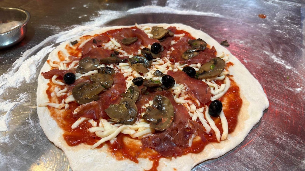 A pizza with pepperoni, mushrooms, olives, and green peppers on a floured surface. 2