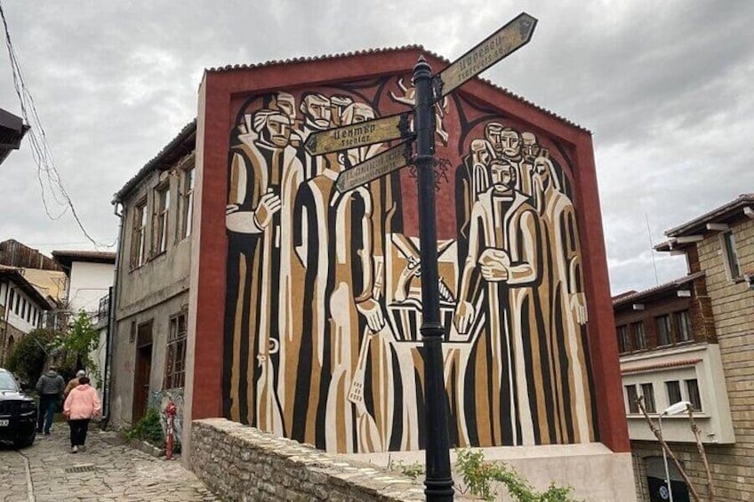 A mural on a building with abstract figures and a street sign. 4