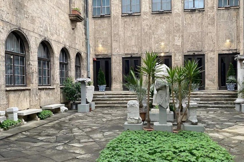 A courtyard with stone flooring, potted plants, and a statue. 3