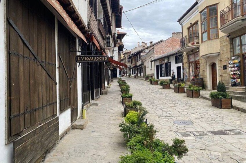 A cobblestone street lined with traditional buildings, a sign for 'LUKIAKIAKIS,' and potted plants. 2