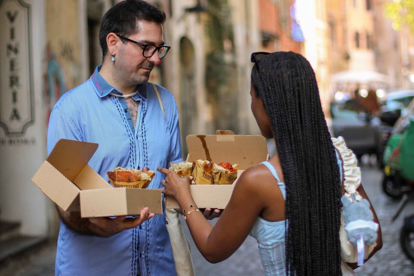 Two people exchanging pizza boxes on a street. 2