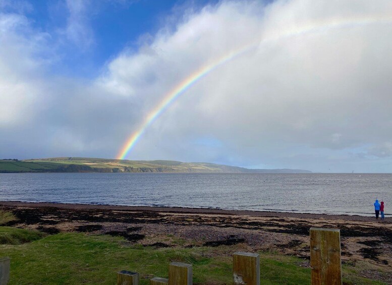 A coastal landscape with a rainbow over the sea and people on the shore. 1