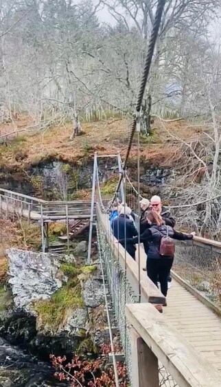 A suspension bridge with metal railings and wooden planks, surrounded by rocky terrain and sparse vegetation. 2