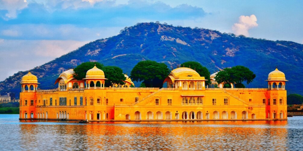 A yellow palace with multiple domes, situated by a calm lake with mountains in the background. 4