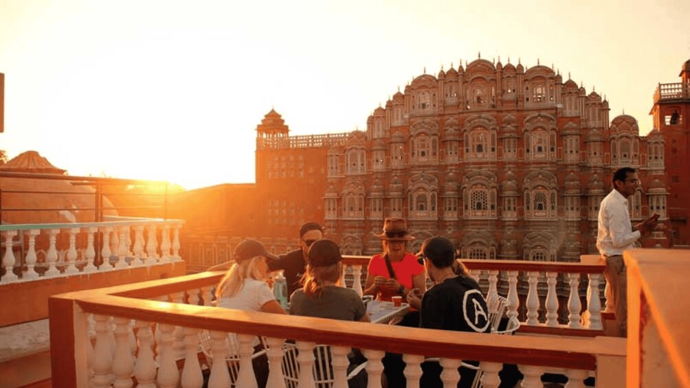 A group of people sitting on a balcony with a large, ornate building in the background. 5