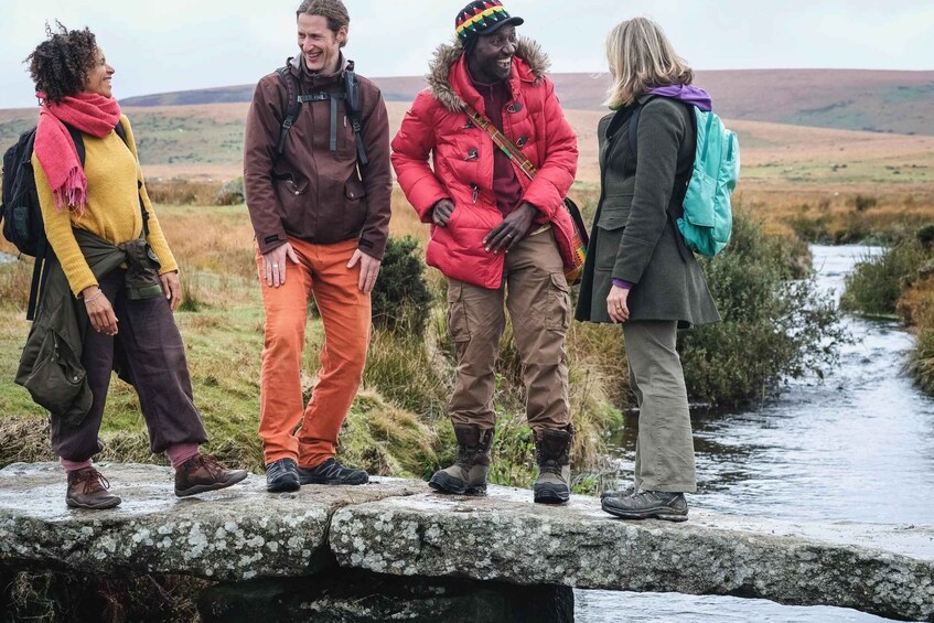 Four people standing on a stone bridge over a stream in a grassy landscape. 4
