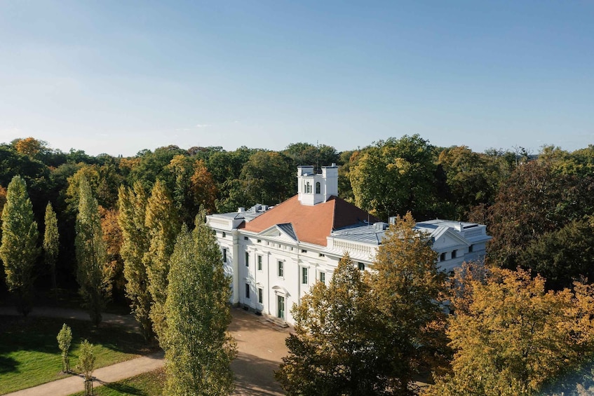 A large white building with a red roof, surrounded by trees and a clear sky. 2