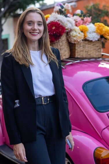A person standing in front of a pink car with a basket of flowers on the roof. 2