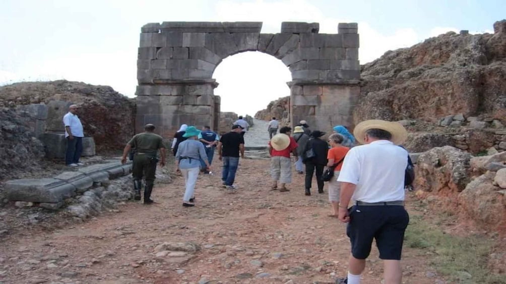 A group of people walking towards a large stone archway in a historical site. 4