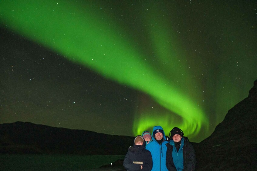 Three people standing under a green aurora display. 2