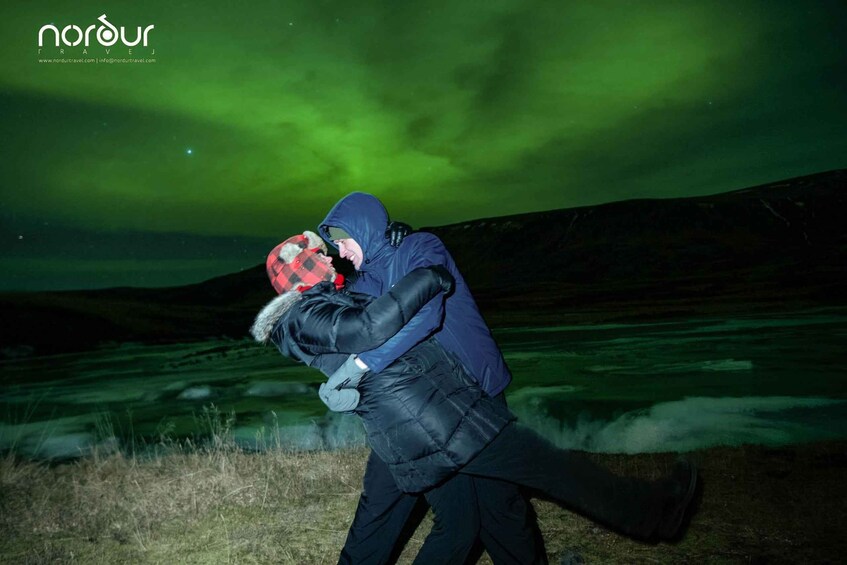 Two people embracing under a green aurora borealis. 4