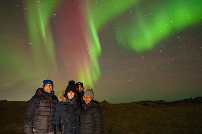 Three people standing in a snowy landscape under a night sky with green aurora borealis. 5