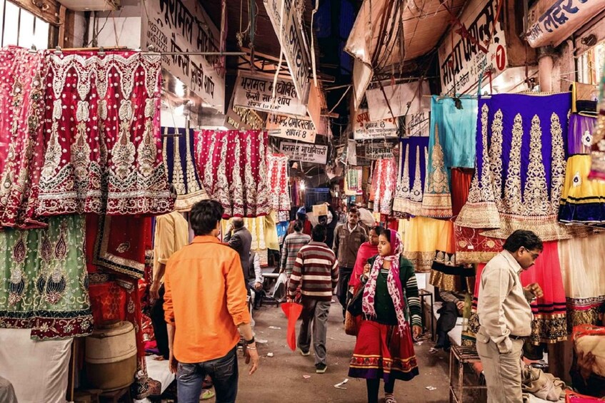A crowded market with colorful fabrics and traditional clothing on display. 2