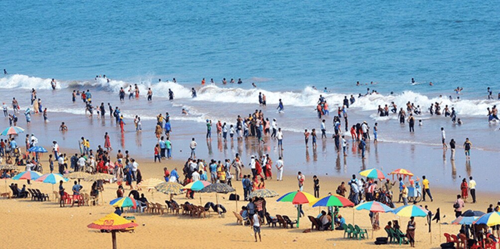 A crowded beach with people swimming and sunbathing under colorful umbrellas. 2