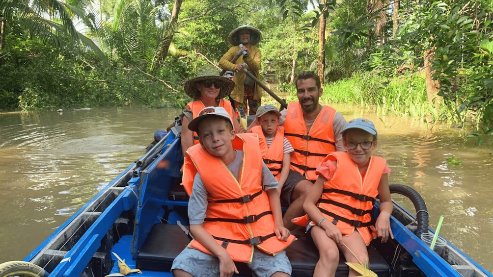 A group of people in a boat wearing life jackets, surrounded by dense greenery and water. 4