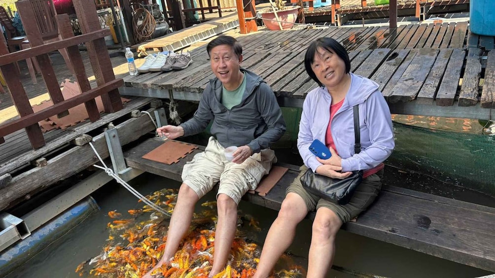 Two people sitting on a wooden dock by a koi pond. 2