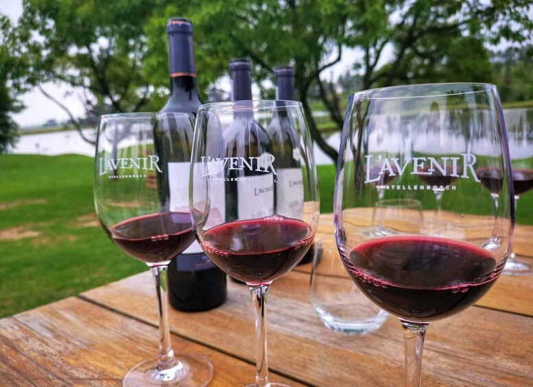 Three wine glasses with LAVENIR wine on a wooden table, with bottles in the background and a lake view. 5