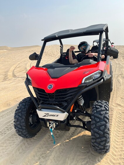 A red off-road vehicle with large tires on a sandy terrain. 3
