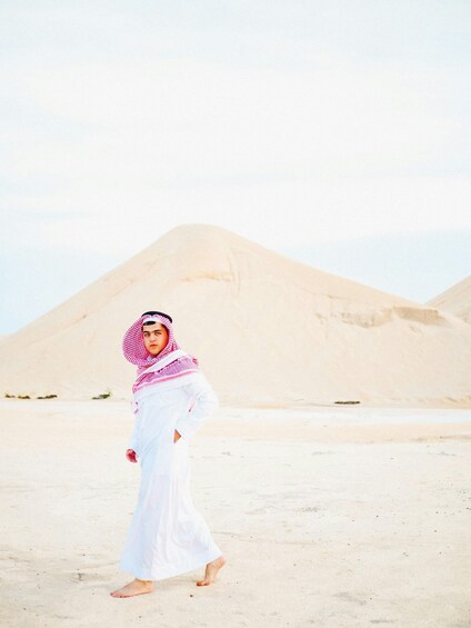 A person in traditional attire walking on a desert with sand dunes in the background. 4