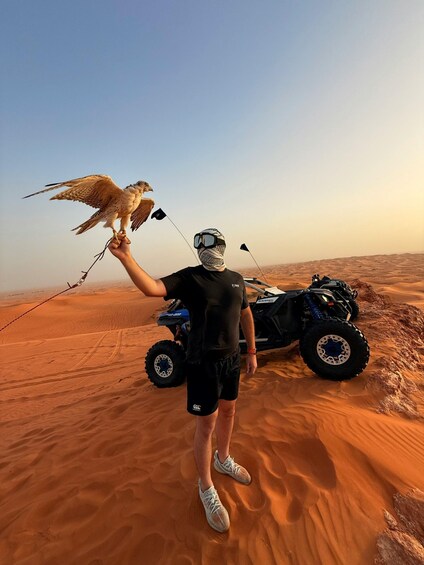 A person holding a bird of prey in a desert with a dune buggy in the background. 5