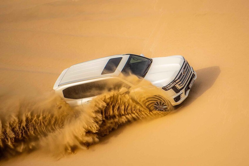 A white SUV driving through a sandy desert landscape. 1