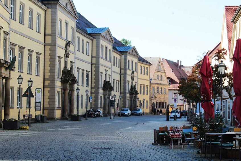 A cobblestone street lined with historic buildings, outdoor seating, and parked cars. 5