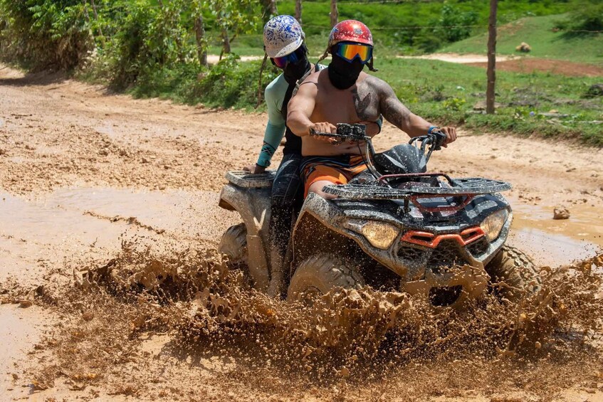 Two people on a quad bike driving through a muddy area. 2