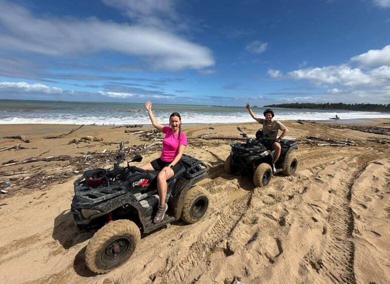 Two people on ATVs on a sandy beach with the ocean in the background. 4
