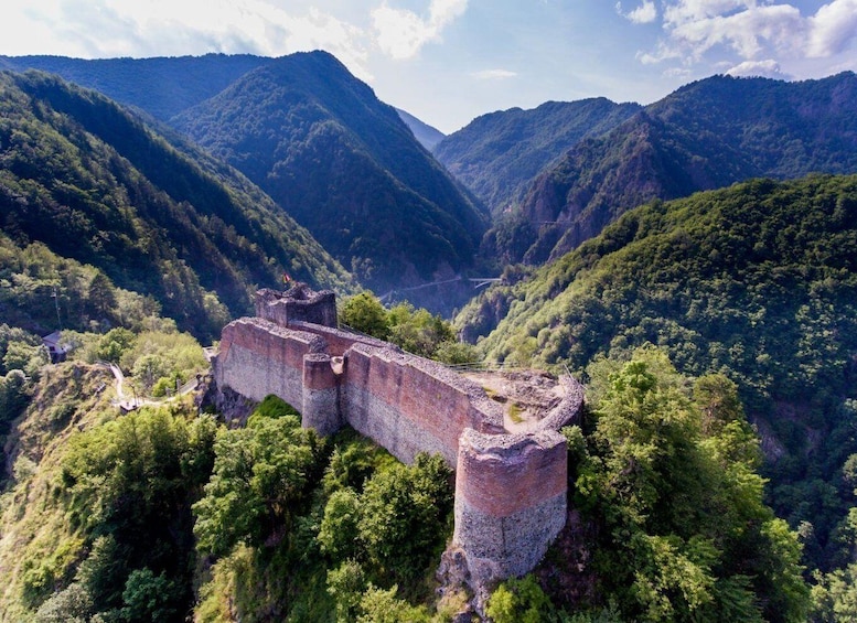 A historical stone fortification surrounded by lush green mountains and a valley. 3