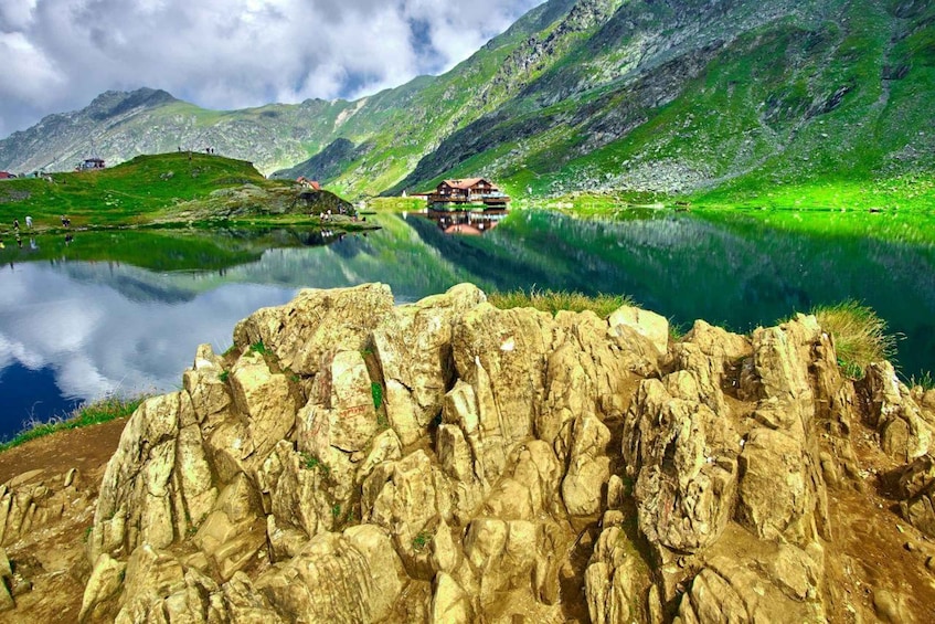 A mountain lake with a house on the shore, rocky foreground, and green hills. 2