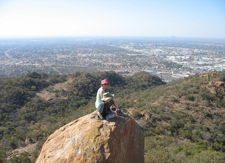 A person sitting on a rock with a cityscape in the background. 1