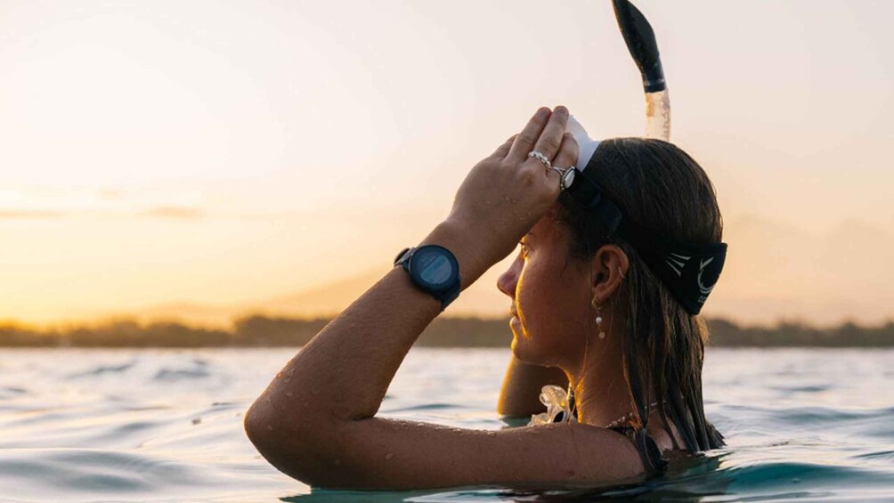 A person snorkeling with a snorkel and mask, wearing a watch, in a body of water during sunset. 2